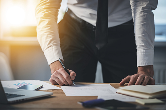 Close-up part of young man signing documents while standing at his working place